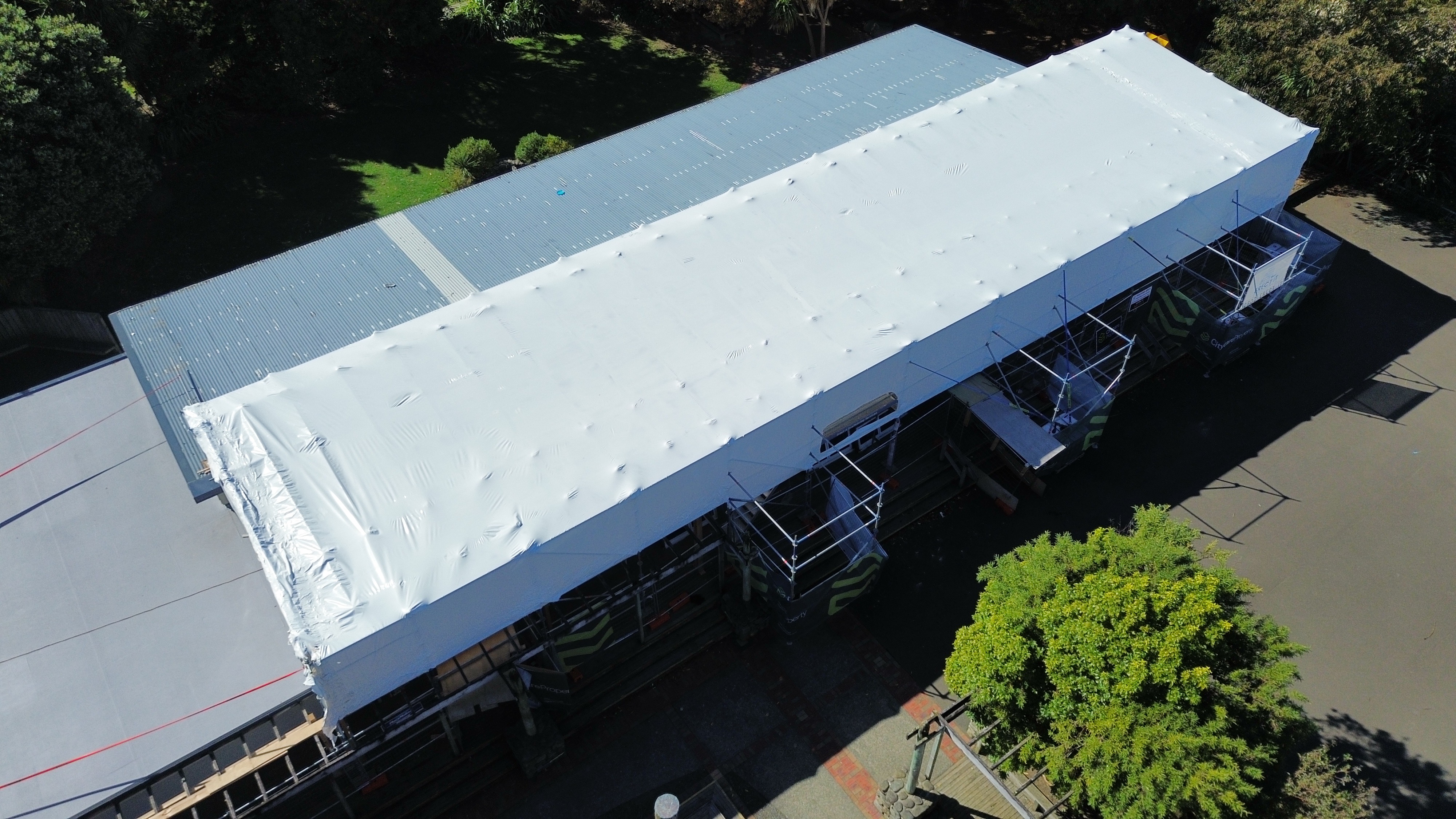 Scaffold shrinkwrap fully installed over Avalon Primary School classroom block, Lower Hutt — aerial drone view