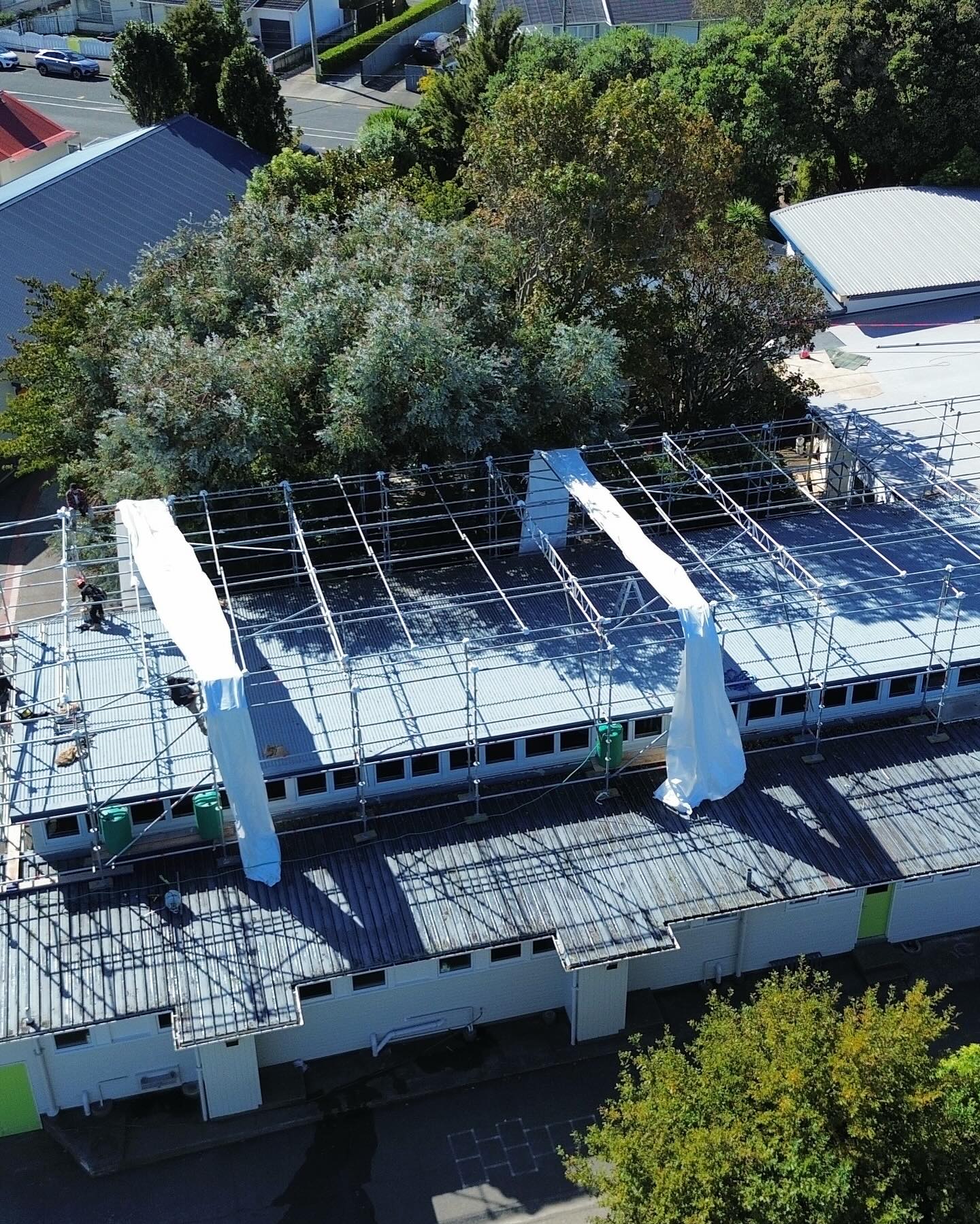 Aerial view of scaffold shrinkwrap temporary roof frame being installed over Avalon Primary School in Lower Hutt — Erect It Scaffolding crew on site during asbestos removal project