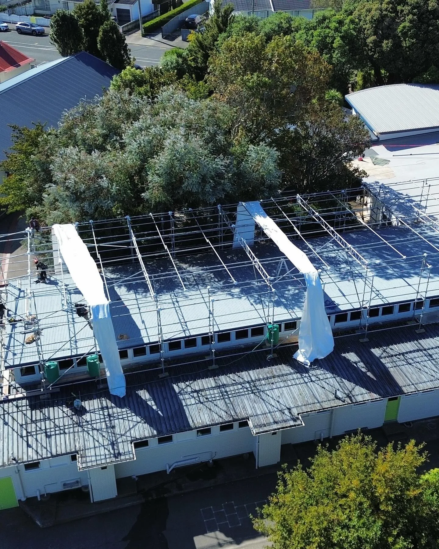Aerial view of scaffolding shrinkwrap temporary roof frame being installed over Avalon Primary School in Lower Hutt — Erect It Scaffolding crew on site during asbestos removal project