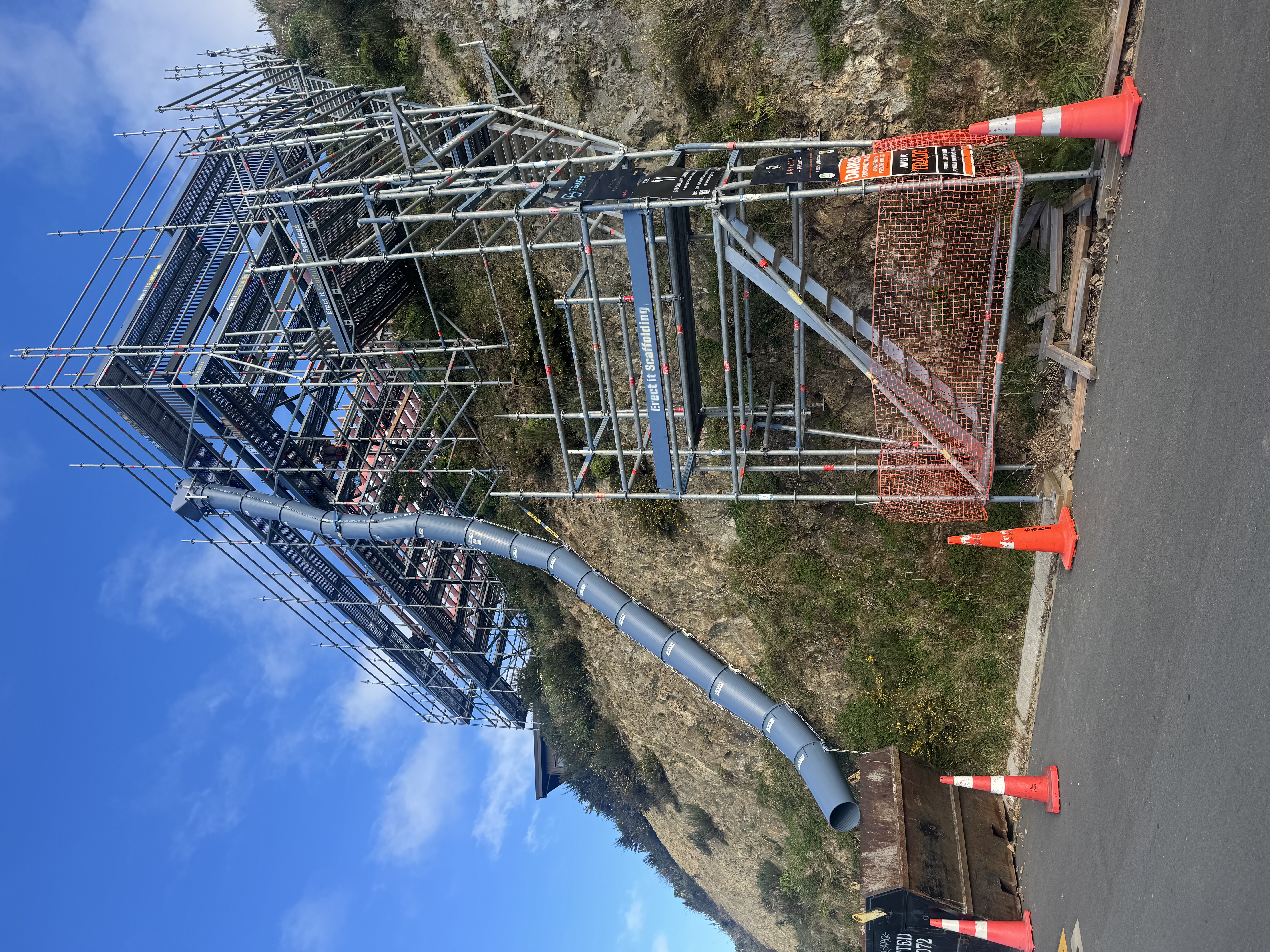 Erect It Scaffolding steep hillside residential scaffold in Island Bay Wellington — featuring rubbish chute running down the cliff face, stair access tower and loading bay at road level