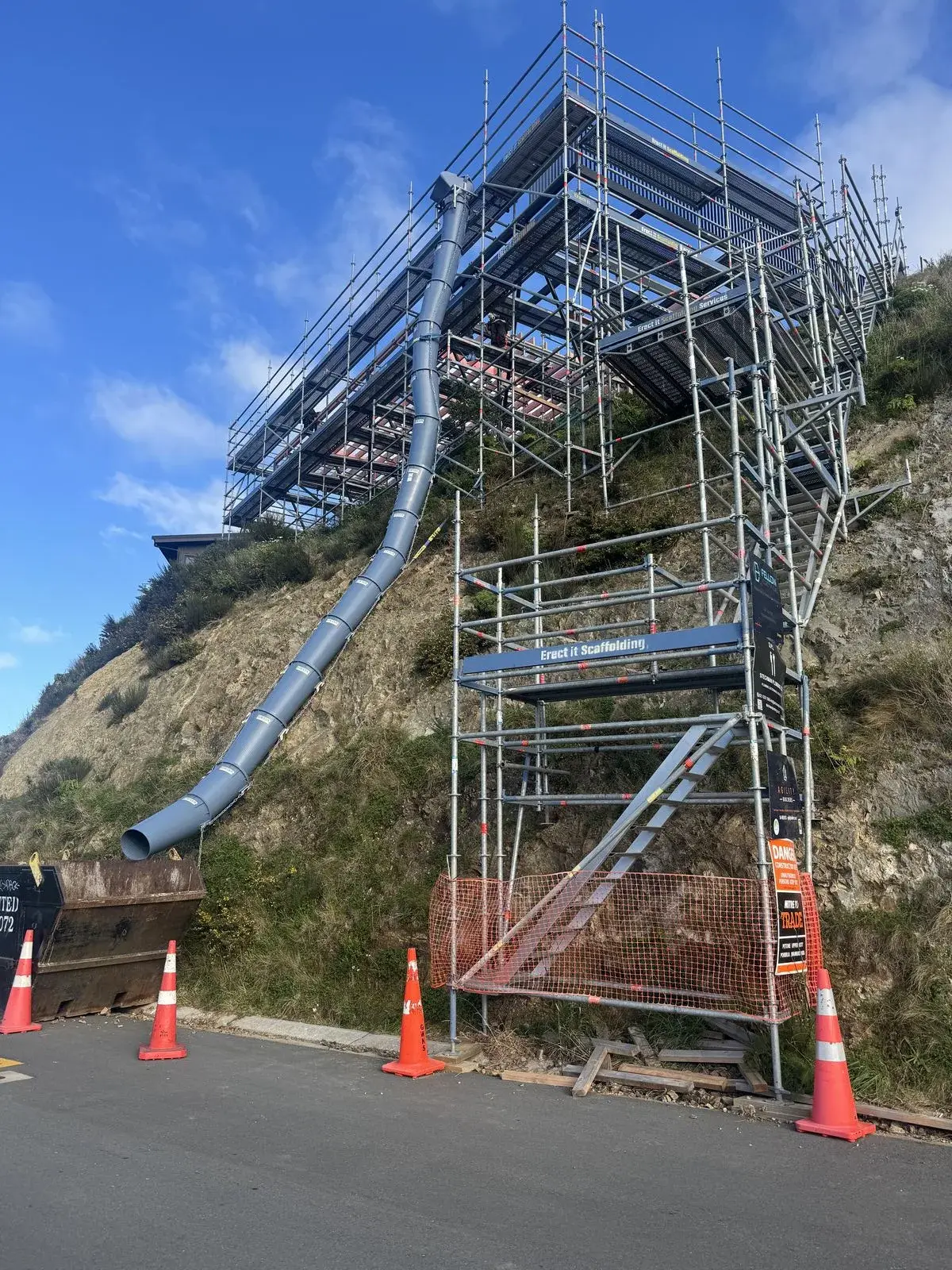 Erect It Scaffolding steep hillside residential scaffolding in Island Bay Wellington — featuring rubbish chute running down the cliff face, stair access tower and loading bay at road level