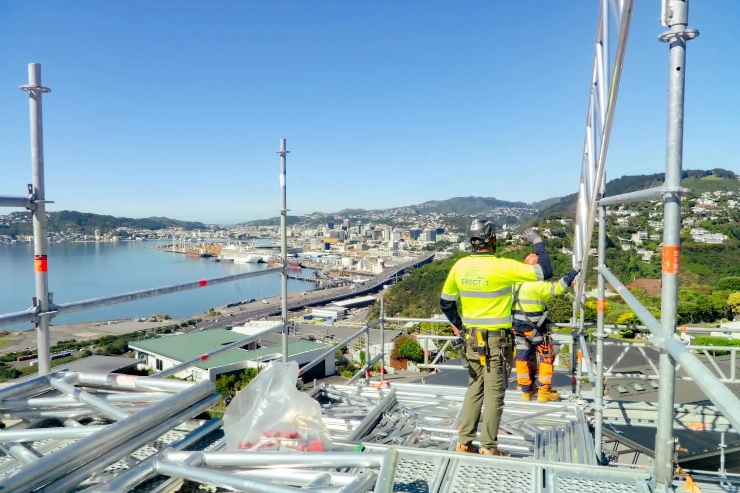 Erect It Scaffolding crew installing a Dessa temporary roof system in Khandallah, Wellington — panoramic view over Wellington Harbour and CBD