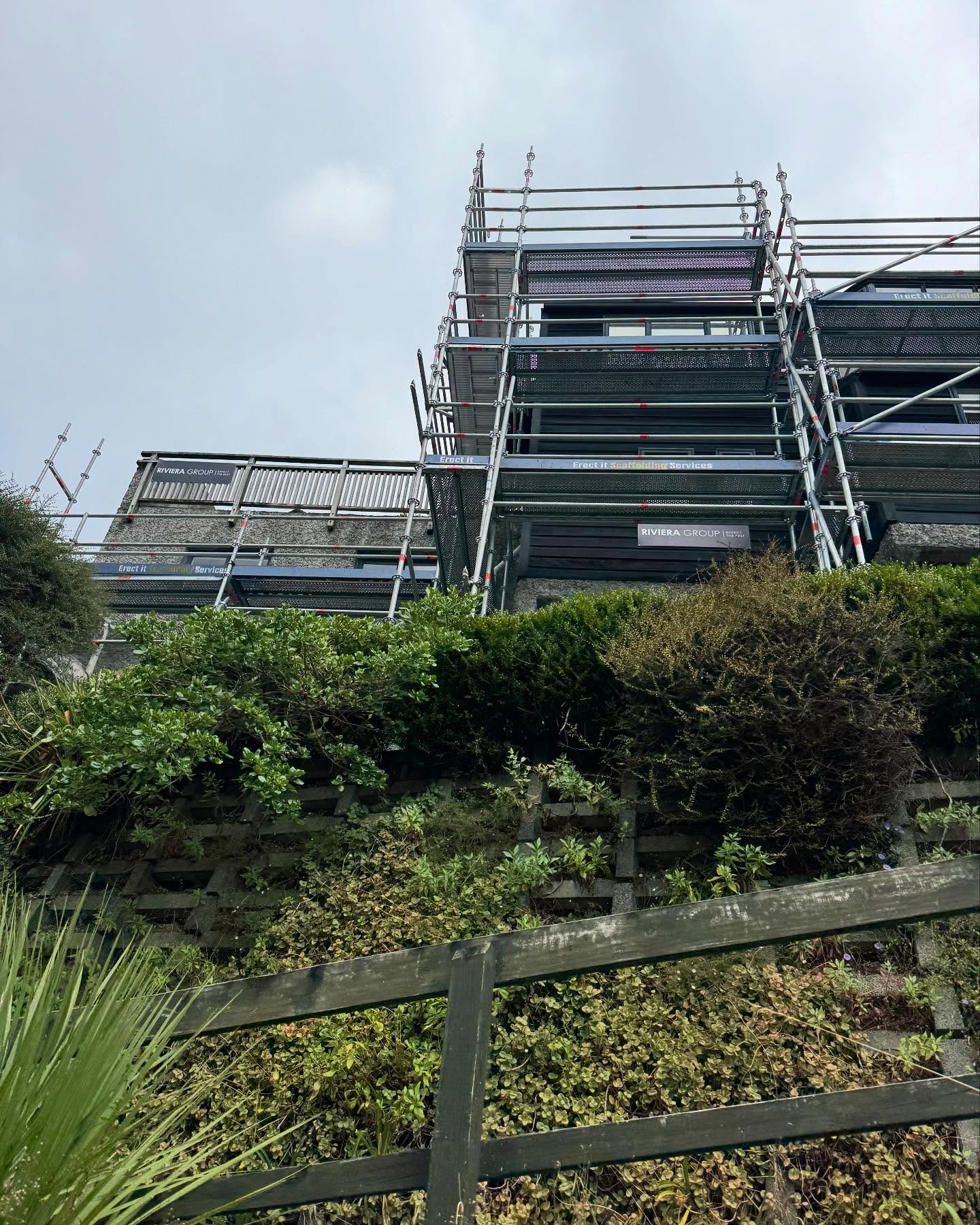 Multi-level scaffold erected by Erect It Scaffolding on a steep hillside property in Oriental Bay / Mt Victoria, Wellington — Erect It and Riviera Group banners visible across the full height of the complex multi-level structure