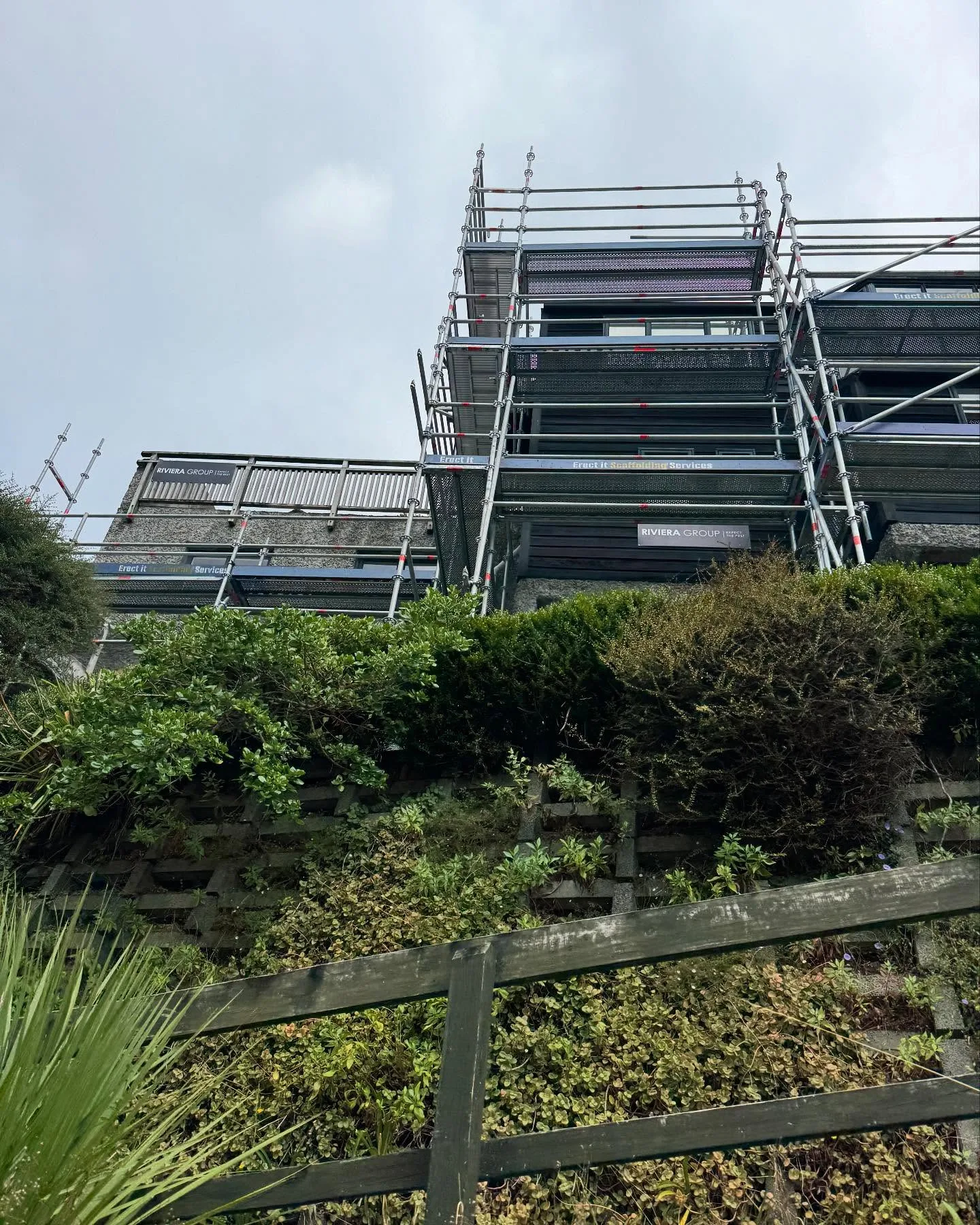 Multi-level scaffolding erected by Erect It Scaffolding on a steep hillside property in Oriental Bay / Mt Victoria, Wellington — Erect It and Riviera Group banners visible across the full height of the complex multi-level structure