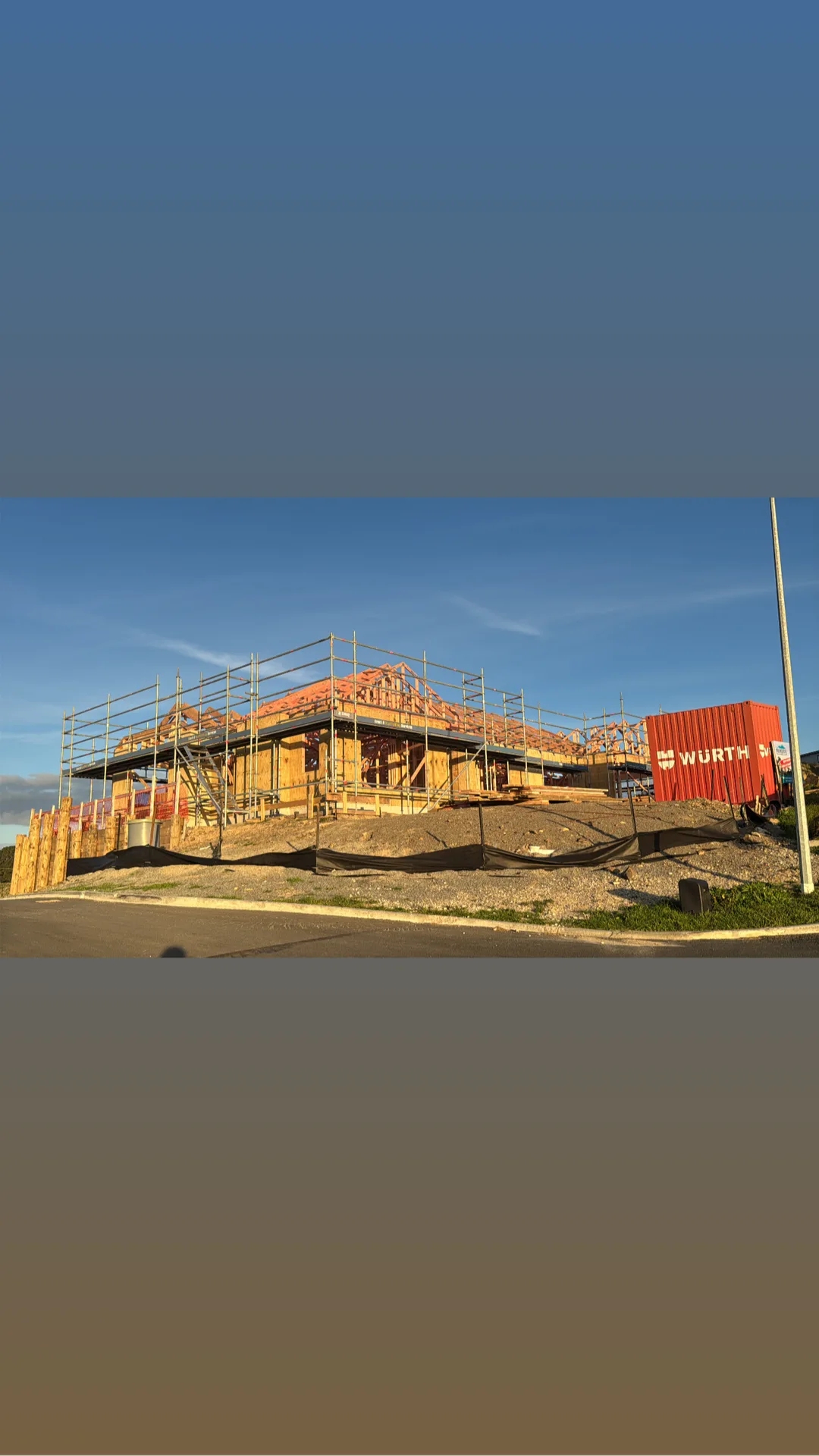 Erect It Scaffolding around a new residential build at the framing stage — full perimeter scaffolding at golden hour with blue sky, Würth shipping container on site