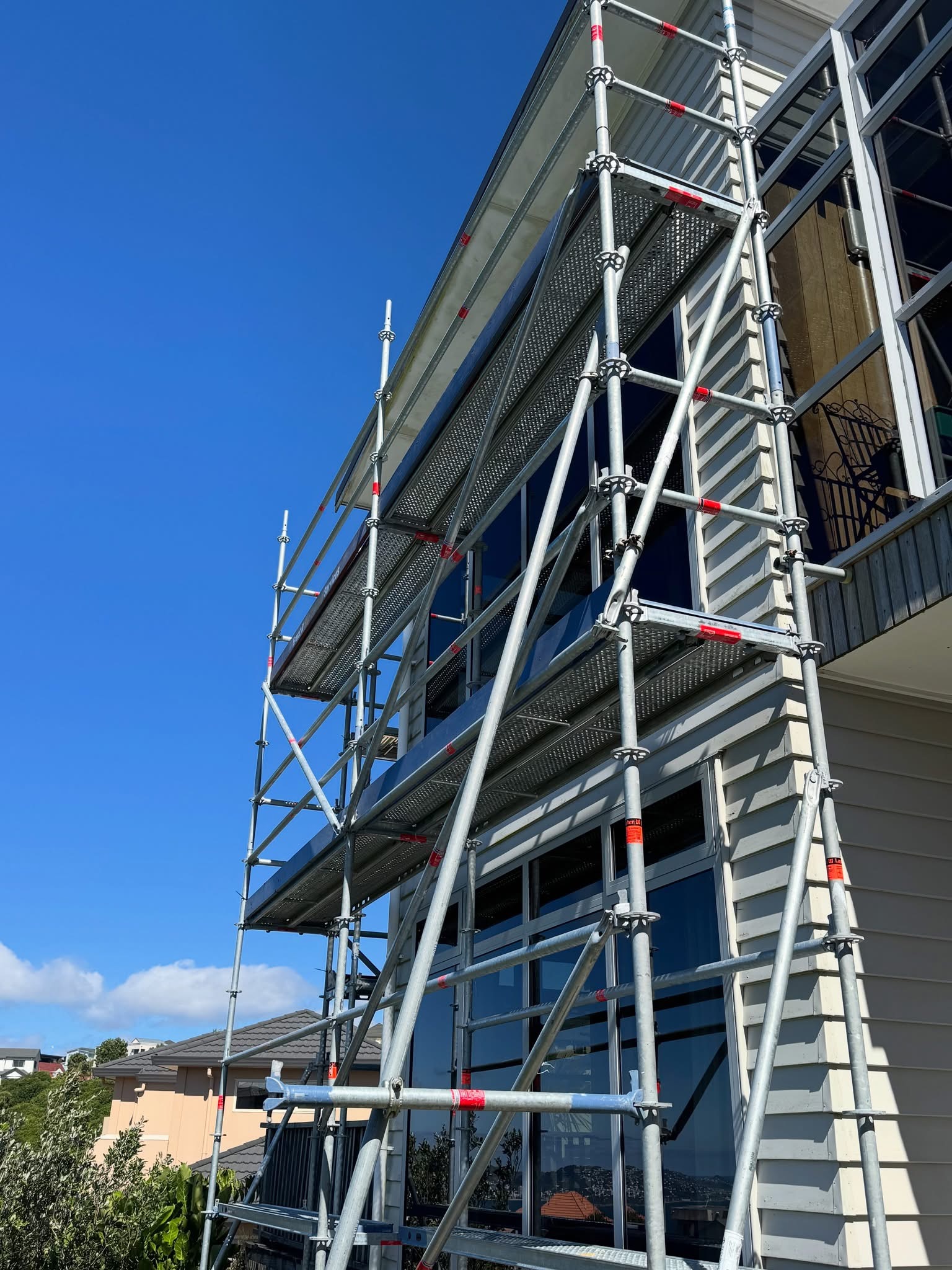 Multi-level Ringlock scaffolding erected on the motorway-facing elevation of a residential home in Newlands, Wellington — clean decked platforms providing safe access for exterior repaint and rotten weatherboard repairs