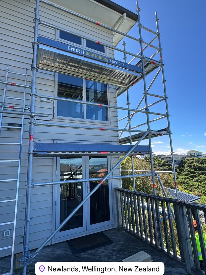 Erect It Scaffolding branded board on residential scaffolding in Newlands, Wellington — multi-level access platform for full exterior repaint with Wellington Harbour visible in the background