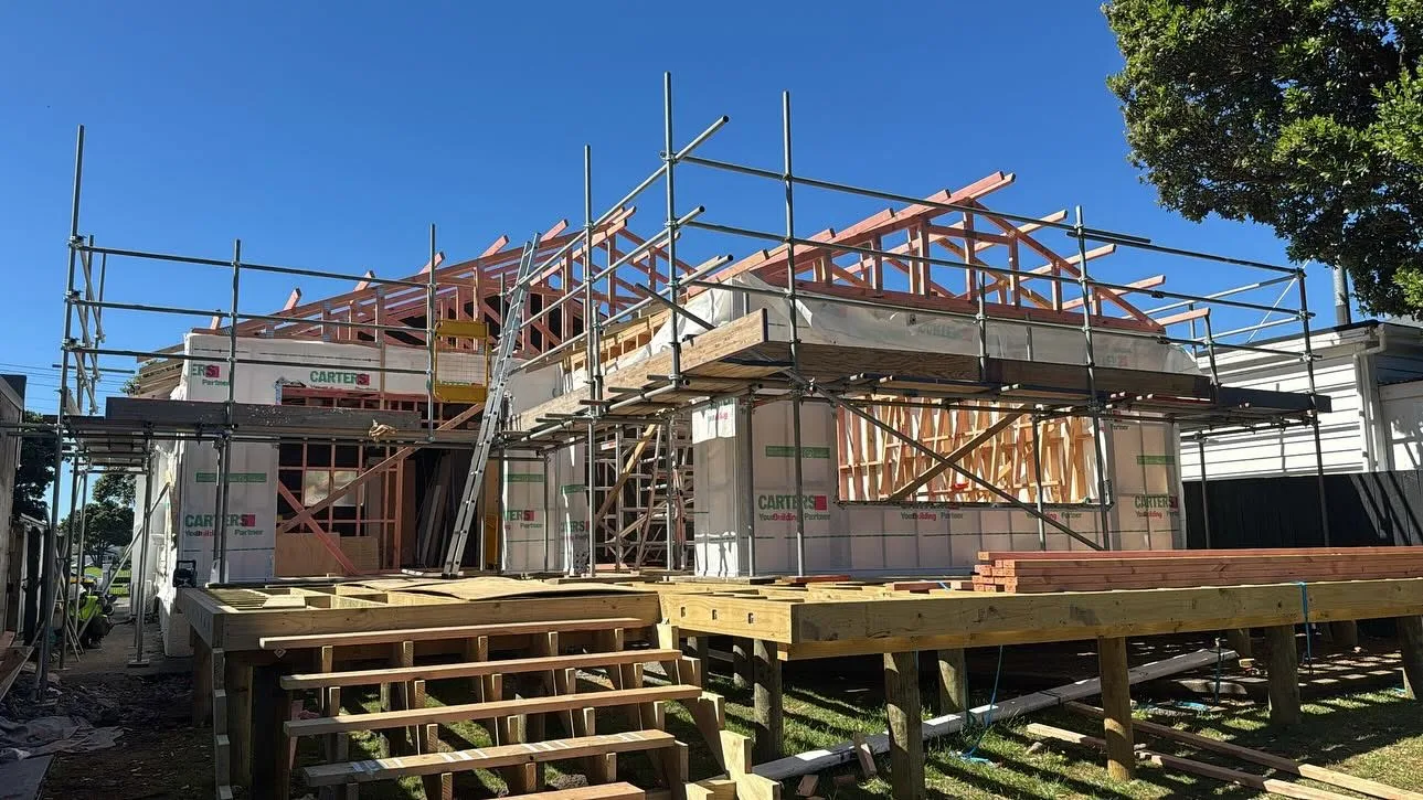 Tube and clip scaffolding erected by Erect It Scaffolding around a residential extension at framing stage in Seatoun, Wellington — Carters building materials on site, clear blue sky