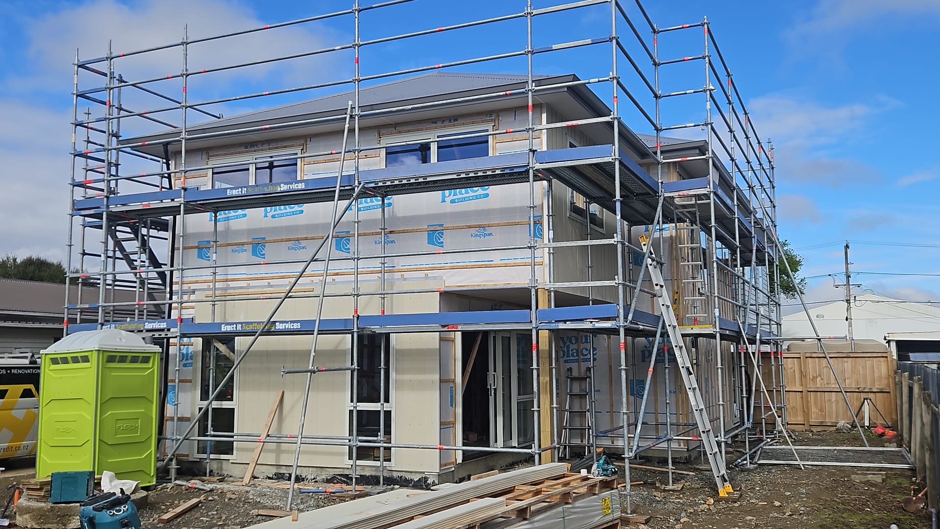 Full multi-level scaffolding on a new residential build in Trentham, Upper Hutt at cladding stage — Erect It Scaffolding branded boards visible across front and side elevations, Kingspan insulation and YourPlace wrap on building