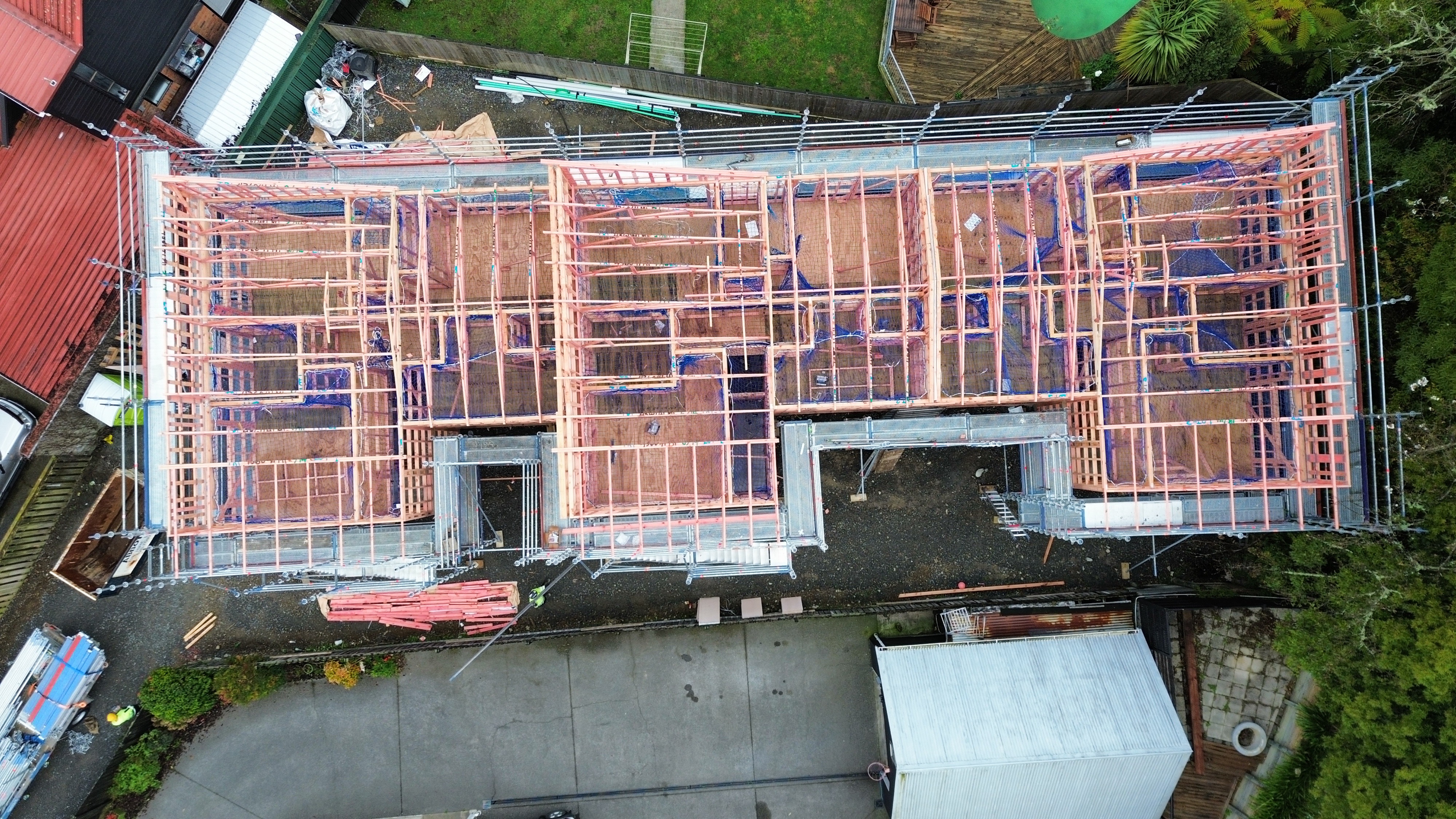 Aerial drone view of Trentham Upper Hutt new residential build at framing stage — scaffolding perimeter wrapping entire footprint with full timber frame and floor system clearly visible from above, scaffolding crew visible on site